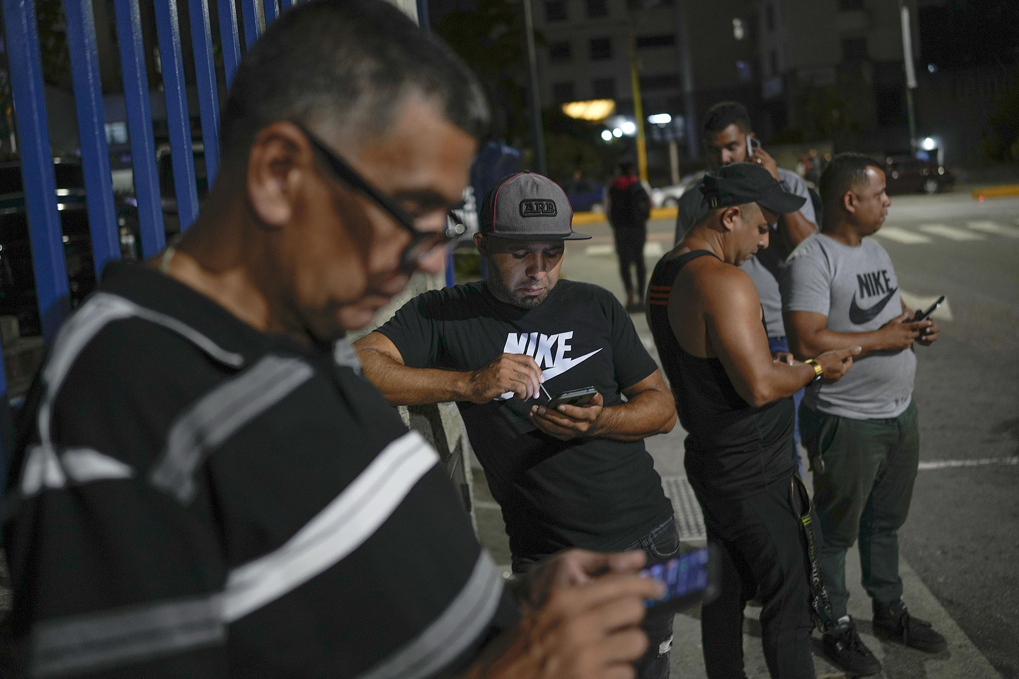 Drivers for a ride-hailing service monitor their cell phones for customers near a shopping mall in Caracas, Venezuela, on May 5, 2022. (Photo by Matias Delacroix/AP)