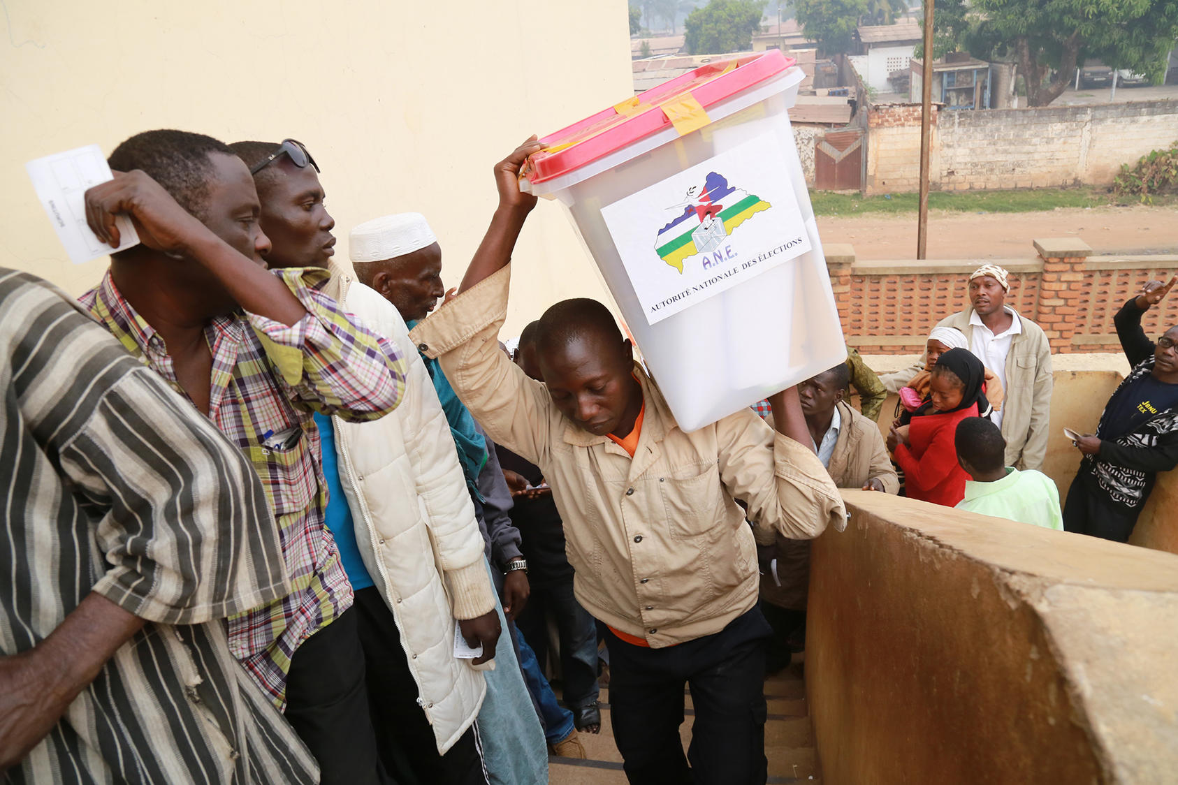 An electoral officer carries election materials into a polling station in Bangui in 2015 as queuing voters look on. (UN Photo/Nektarios Markogiannis)