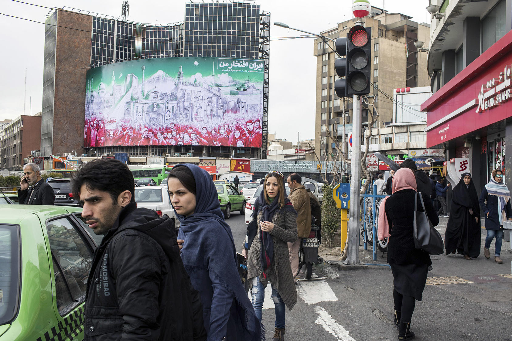 Iranians negotiate Tehran’s traffic in February beneath a mural depicting the 1979 Islamic Revolution. U.S. sanctions, heightened this week, aim to pressure Iran’s government into making broad foreign policy changes. (Arash Khamooshi/The New York Times)