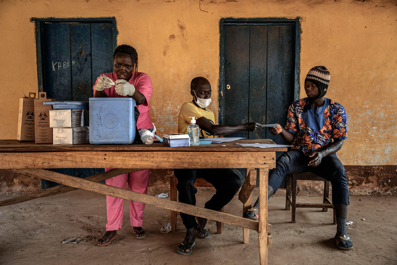 Health workers in Sierra Leone give COVID vaccinations in the village of Kathantha Yimbo, handing blue record cards to vaccinated residents. Mistrust of vaccines is one obstacle to protecting people in fragile states. (Finbarr O'Reilly/The New York Times)