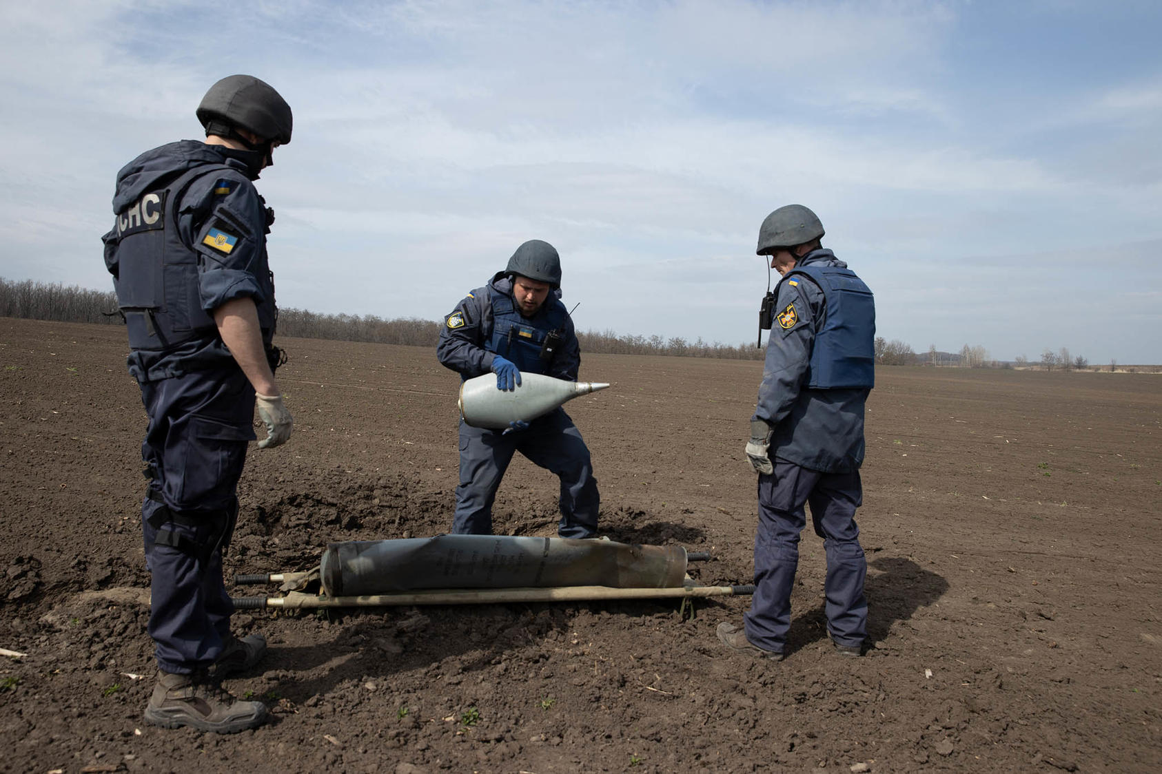 Bomb disposal technicians remove an undetonated rocket loaded with cluster munitions from a field in the village of Ridnyi Krai, Ukraine, April 8, 2022. (Tyler Hicks/The New York Times)