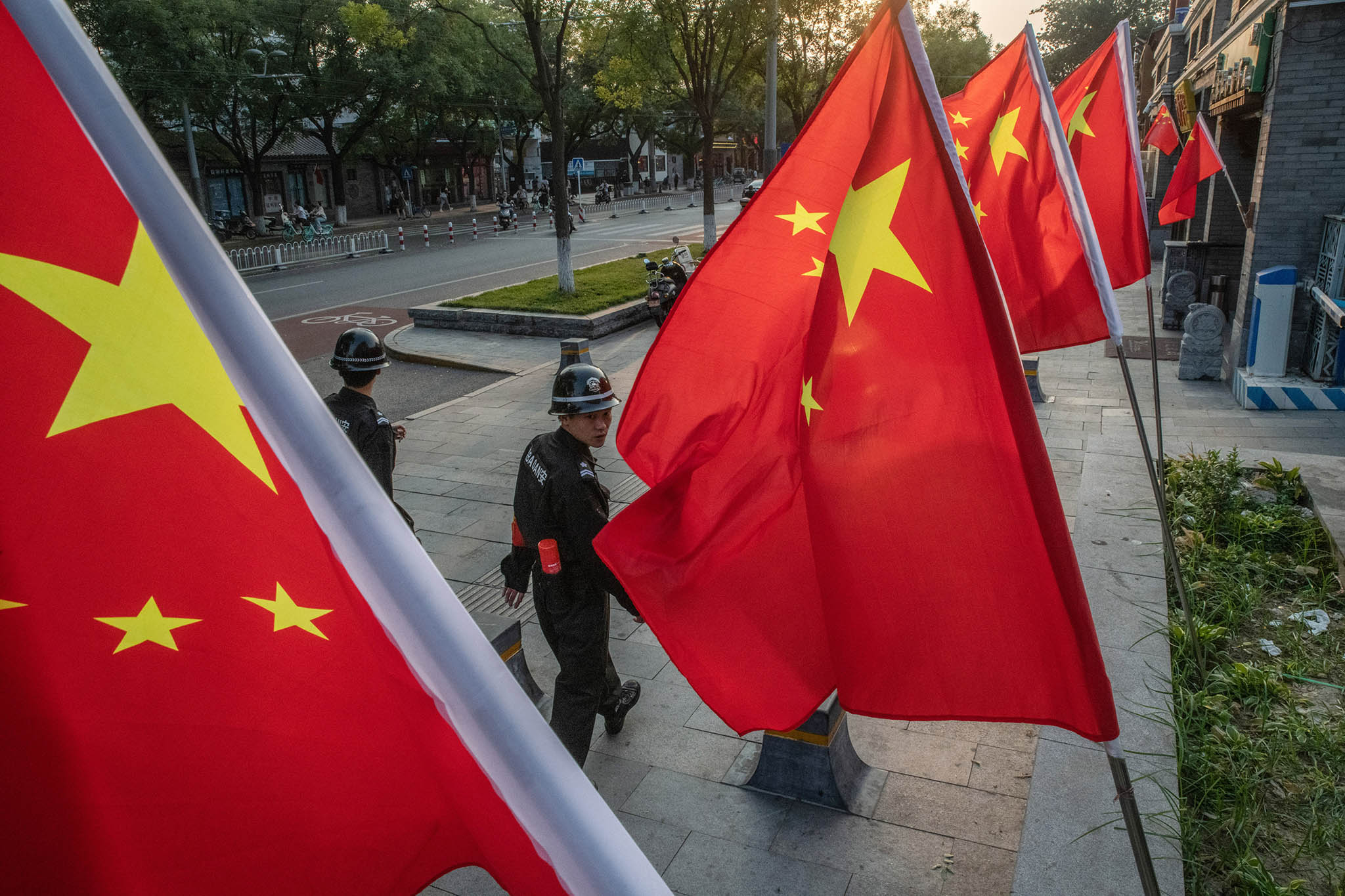 Security guards walking past Chinese flags decorating a street in Beijing. October 1, 2019. (Gilles Sabrie/The New York Times)