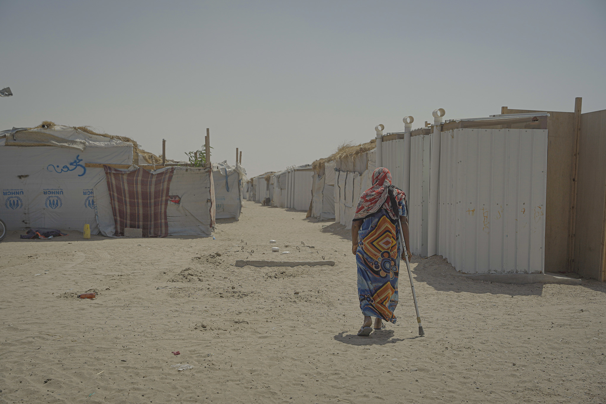 A woman walks with a crutch through a community for displaced persons in Yemen. November 14, 2021. (Muhanad Yasin/European Union)