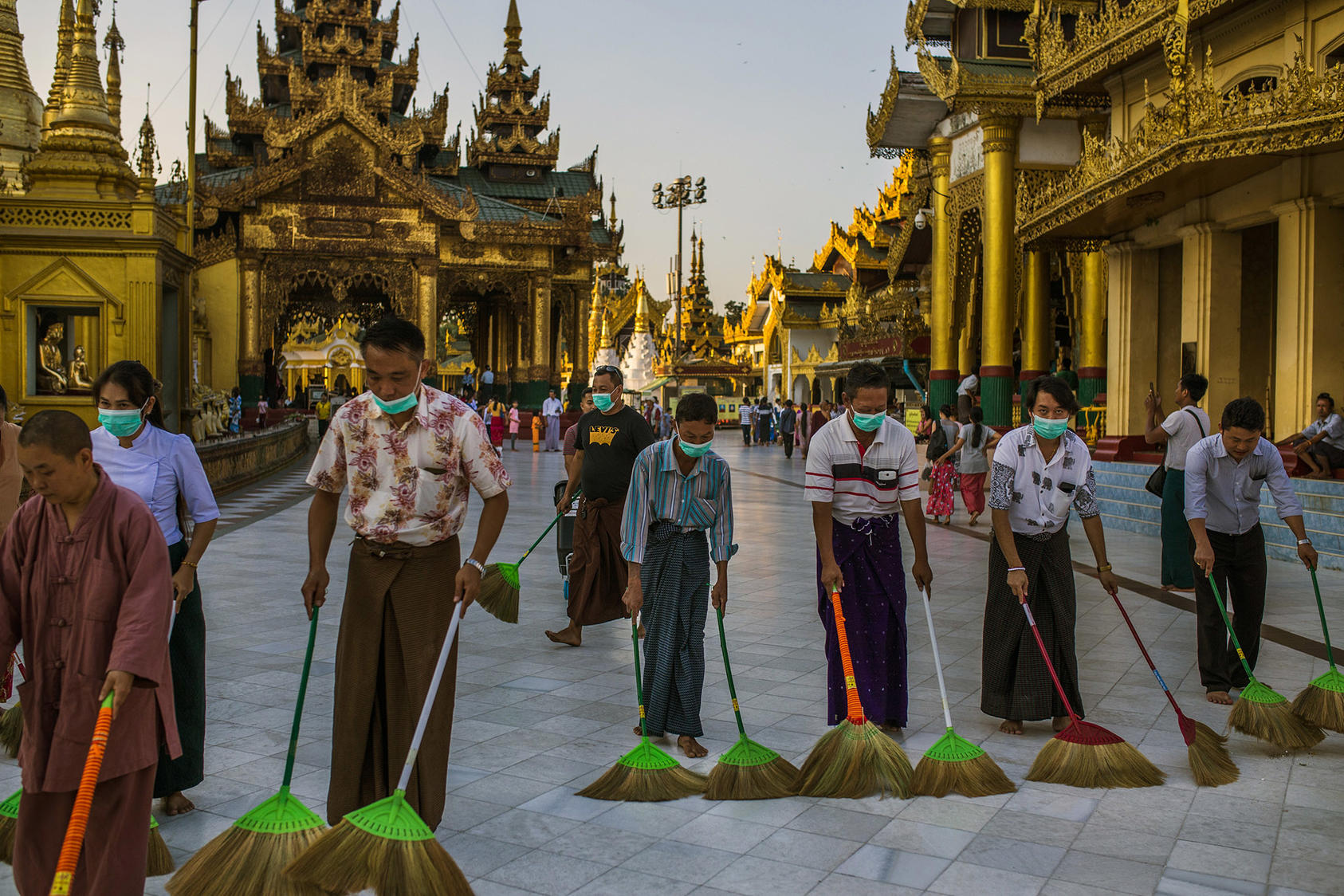 Volunteers, many wearing masks to avoid spreading the COVID19 virus, sweep walkways at the Shwedagon Pagoda, a Buddhist holy site in Yangon, Myanmar, in March. The virus’ spread has since led to the pagoda’s closure. (Minzayar Oo/The New York Times)