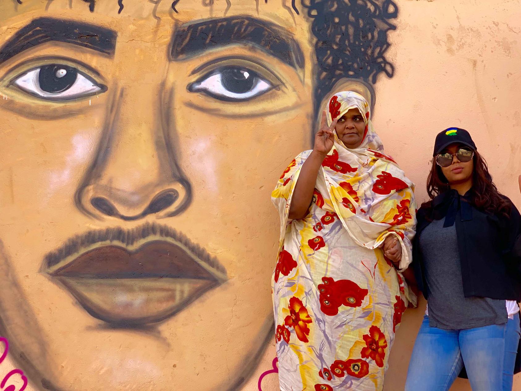 Assil Diab poses with Ahlam Khidr, protest leader and activist, in front of Assil’s mural of Ahlam’s son Hazaa Izzeldine Jaafar, who was killed while peacefully protesting Bashir’s regime in September 2013.