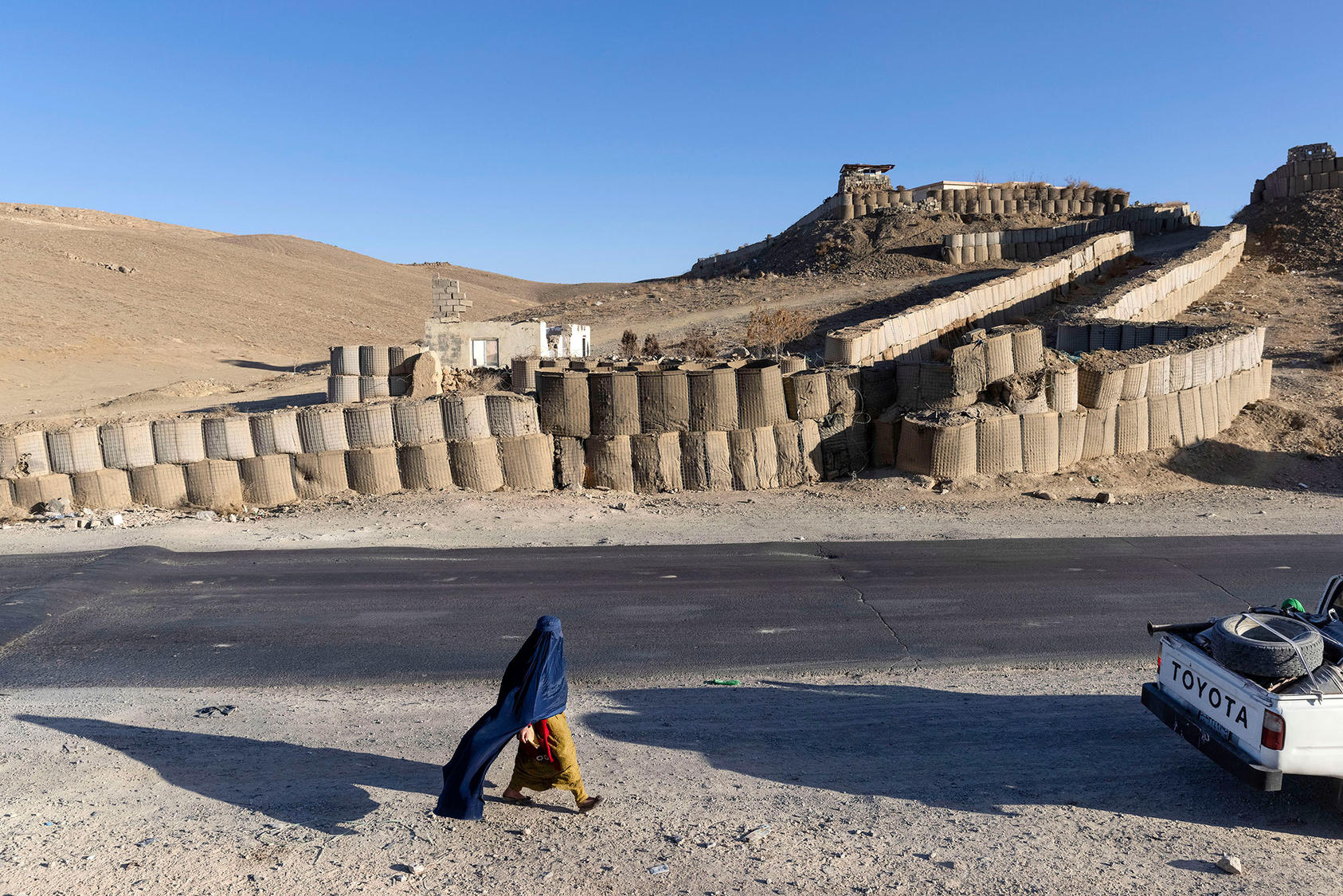 A woman walks along the side of the Kabul–Kandahar Highway north of Ghazni, Afghanistan, in Dec. 8, 2021. (David Guttenfelder/The New York Times)