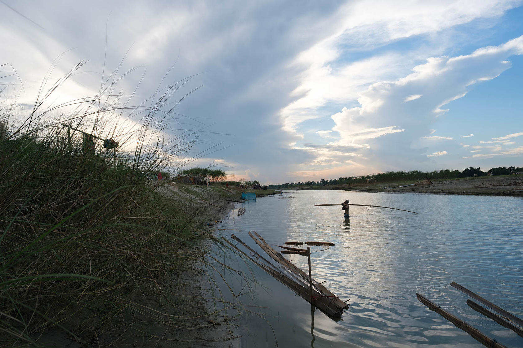 An elderly man carries a bamboo pole and a baby across a stream of the Brahmaputra river, Dholpur, India on Sept. 28, 2021. (Karan Deep Singh/The New York Times)